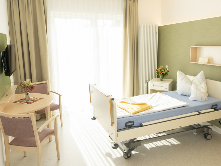 Gästezimmer im Hospiz mit Gästebett, Sitzmöbel und bodentiefen Fenster - Diakonie Hospiz Woltersdorf Gästezimmer im Hospiz mit Gästebett, Sitzmöbel und bodentiefen Fenster - Diakonie Hospiz Woltersdorf