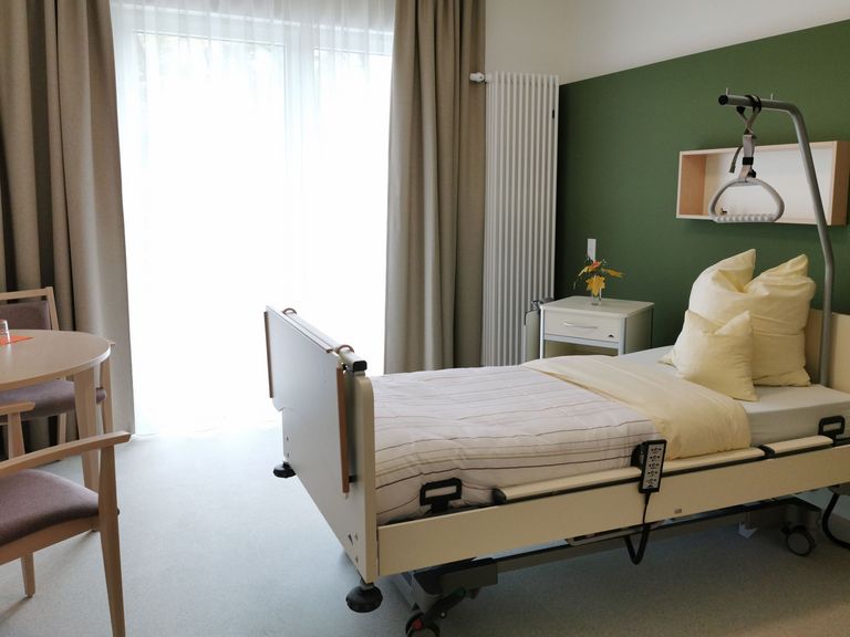 Gästezimmer im Hospiz mit Gästebett, Sitzmöbel und bodentiefen Fenster - Diakonie Hospiz Woltersdorf